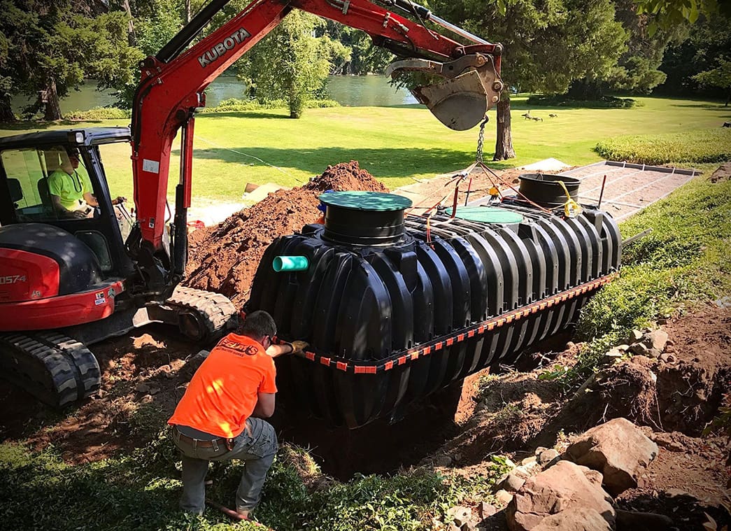 A man working on a black tank in the grass.