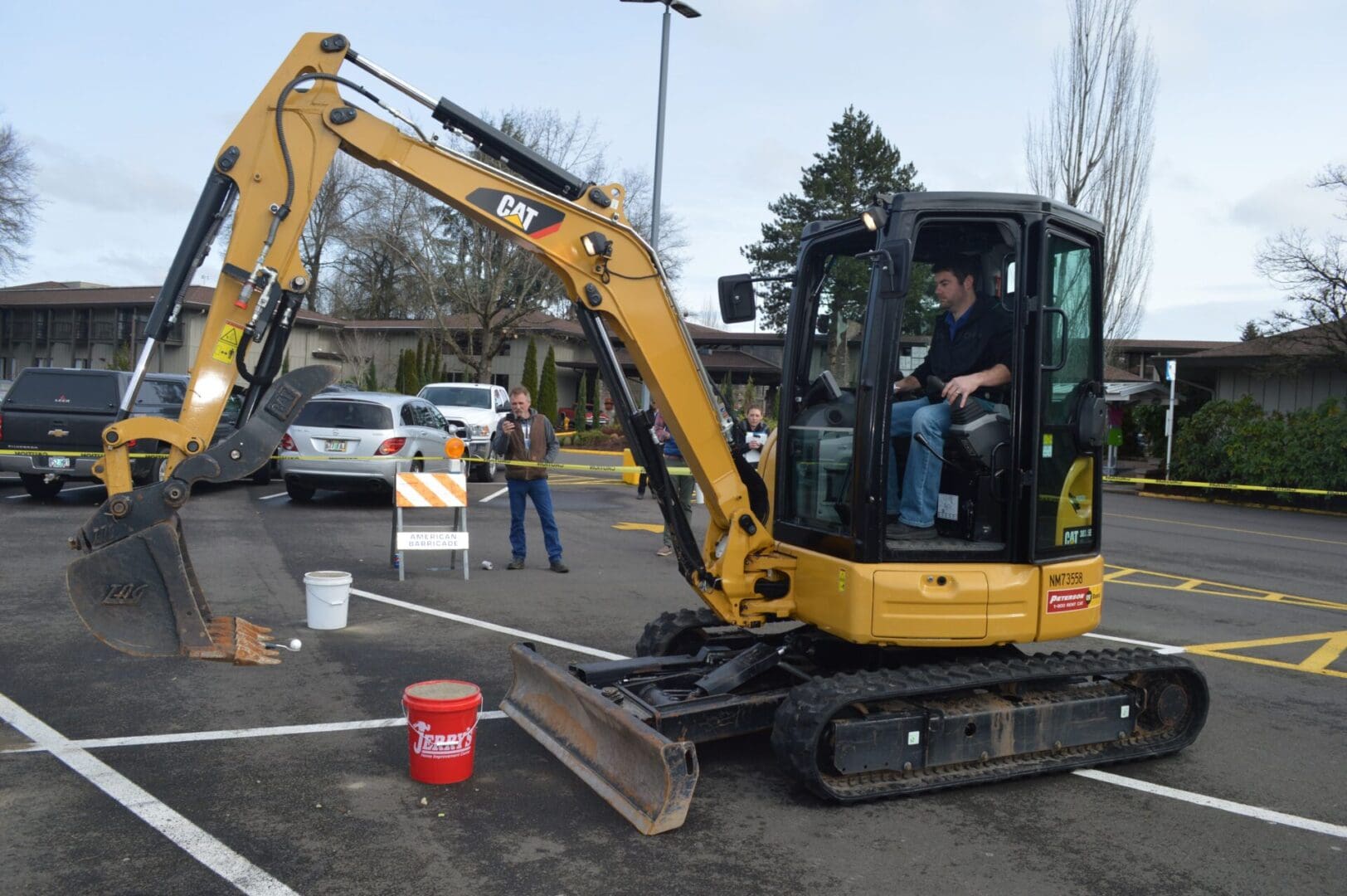 A man driving an excavator in the middle of a parking lot.